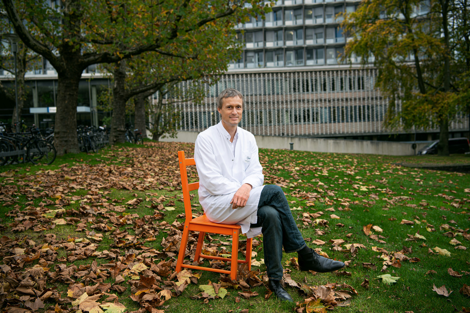 Stefan Roepke sitzt im weissen Kittel auf einem Stuhl vor dem Benjamin Franklin Krankenhaus Berlin