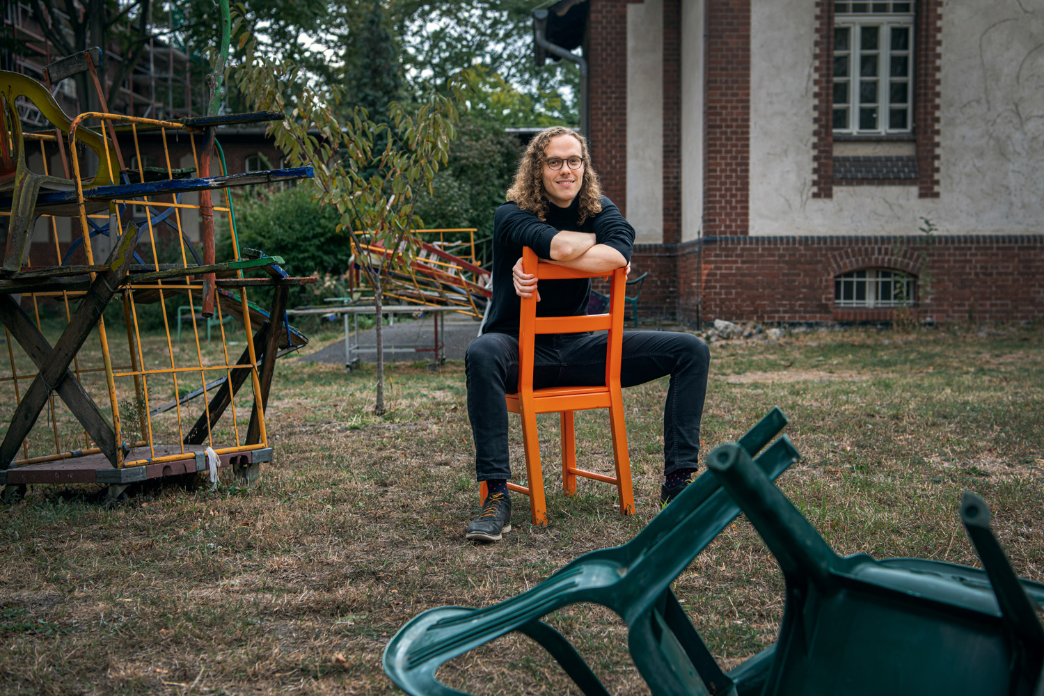 Thomas Chaigne sitzt auf einem Stuhl in einem Garten mit Kunstobjekten auf dem Campus Mitte
