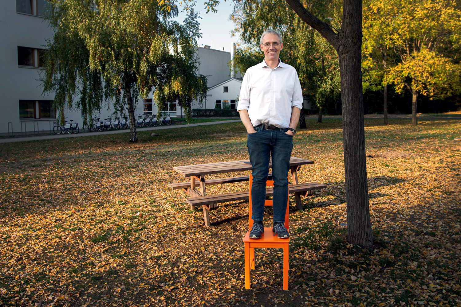 Ulrich Müller von der Jhn Hopkin University steht hemdsarrmlig auf einem Stuhl im Garten des Max delbrueck centrum